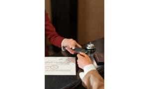 A hotel receptionist handing a key card to a guest. This is travel tip using paper
