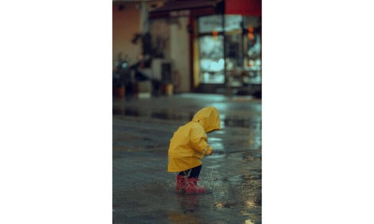 child in raincoat jumping in puddle