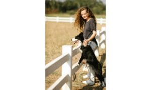 woman and her border collie dog leaning against a white fence