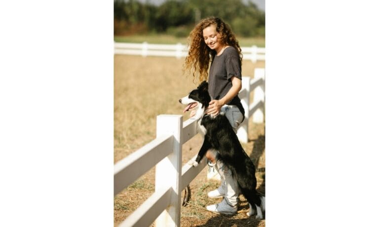 woman and her border collie dog leaning against a white fence