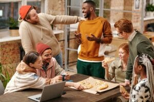 Multiracial group of people by the table conversing as solo travellers in hostel