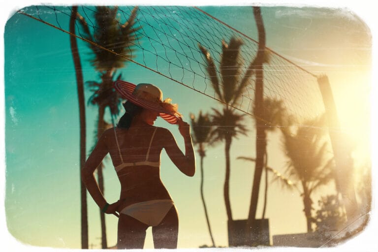 Photo in retro style of sexy model girl in white bikini with volleyball net on beach and palms behind blue summer sky