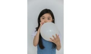 Cute ethnic child inflating white balloon in studio