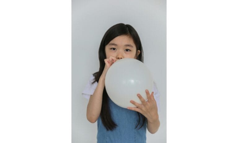 Cute ethnic child inflating white balloon in studio