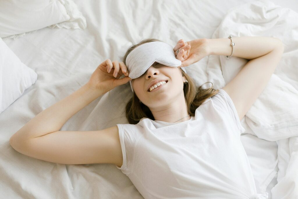 Traveller wearing a soft sleeping mask on a plane seat with dim cabin lighting and a relaxed resting posture
