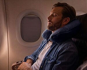 Travel neck pillow resting on an airplane seat with a suitcase nearby showing U-shaped and compact designs for head and neck support