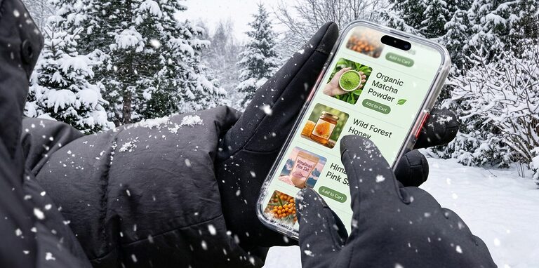A pair of travel gloves placed beside a backpack and phone, showing touchscreen use and compact packing for cold weather trips