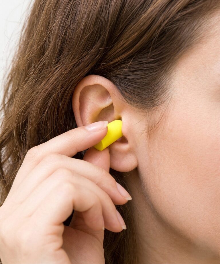 A set of foam and silicone ear plugs placed beside a travel pillow and eye mask on an aeroplane tray table