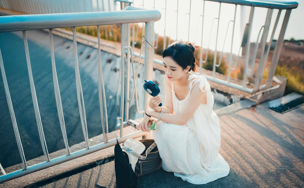 Traveller holding a compact portable handheld fan outdoors in warm weather showing airflow use during a sunny day trip