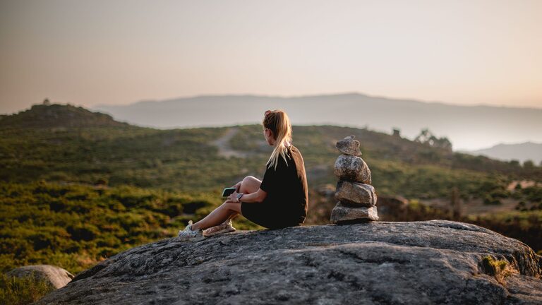 Solo traveller sitting on a hilltop overlooking a mountain landscape