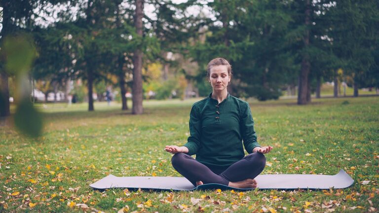 Woman meditating alone in a peaceful outdoor retreat setting surrounded by greenery