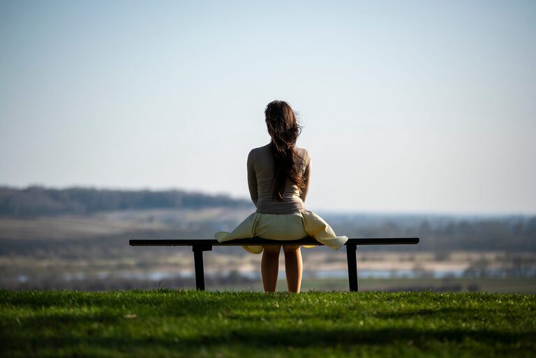 Solo traveller sitting quietly on a bench overlooking a scenic field, symbolizing solitude and reflection.