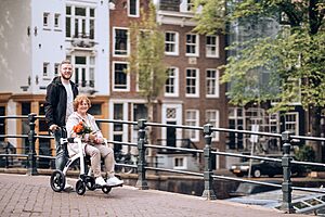 A senior woman in a wheelchair with flowers enjoys a stroll along Amsterdam's iconic canals.