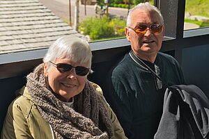 A happy senior couple wearing sunglasses and smiling, enjoying a sunny day outdoors.