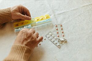 Close-up of hands organising tablets into a weekly pillbox for daily medication management.