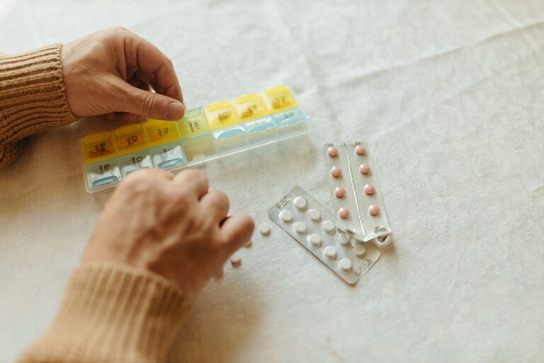 Close-up of hands organising tablets into a weekly pillbox for daily medication management.