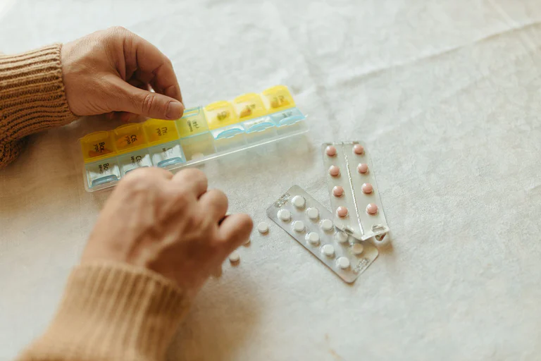 Close-up of hands organising tablets into a weekly pillbox for daily medication management.