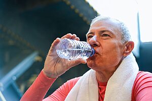 Elderly traveller drinking water with towel around neck in a warm climate