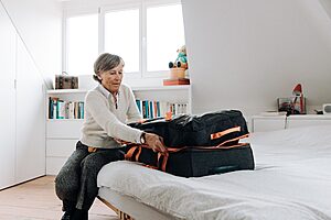 Elderly woman packing suitcase on bed in bright, modern bedroom setting.