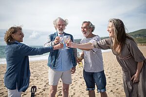 Joyful senior friends clinking glasses and celebrating on a sunny beach in Portugal.