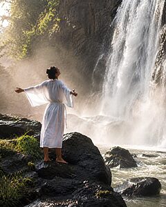 Person standing alone through a waterfall forest on a spiritual travel retreat