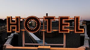 Glowing hotel sign lights up the skyline as evening falls, setting a warm urban scene.