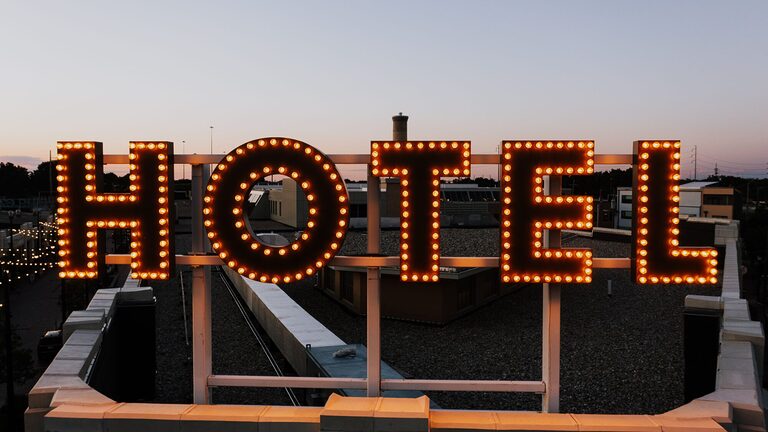 Glowing hotel sign lights up the skyline as evening falls, setting a warm urban scene.