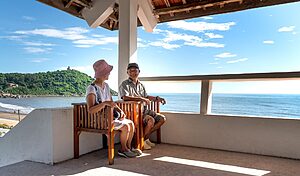 Senior couple sitting on balcony chairs, enjoying a relaxing ocean view in summer.
