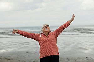 Elderly woman joyfully standing on the beach with open arms