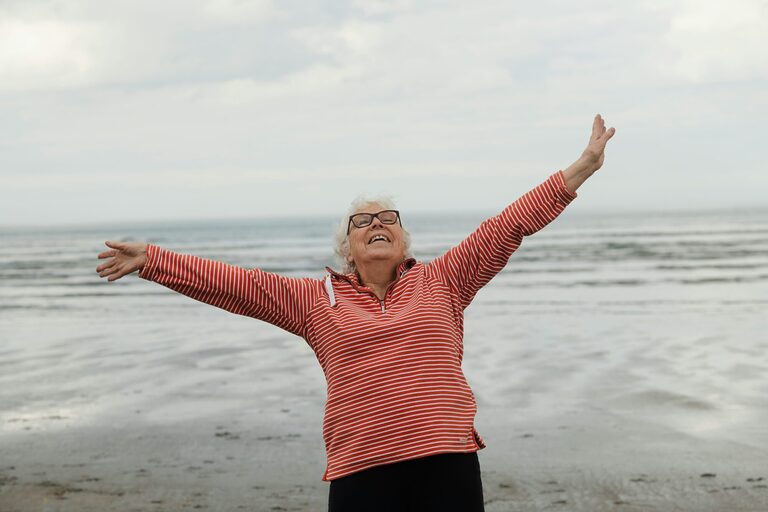 Elderly woman joyfully standing on the beach with open arms