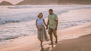 Pregnant couple walking on a beach holiday during their babymoon