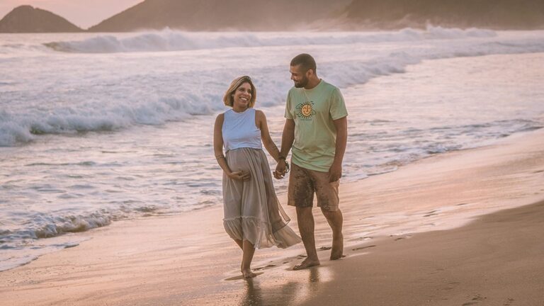 Pregnant couple walking on a beach holiday during their babymoon
