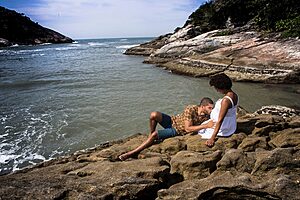 A couple sharing a tender moment by the rocky seaside during a beautiful summer day.