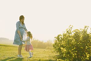 Pregnant mother with daughter enjoying a sunny day outdoors.