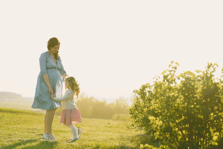Pregnant mother with daughter enjoying a sunny day outdoors.