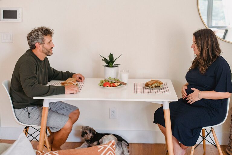 Pregnant woman and partner sharing a home-cooked sandwich lunch with fresh fruit and milk