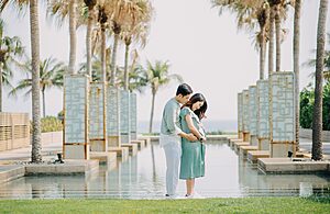 Pregnant couple embraces amidst palm trees reflecting tranquillity and love.