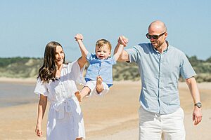 Happy family having fun at the beach, lifting their child in the air.