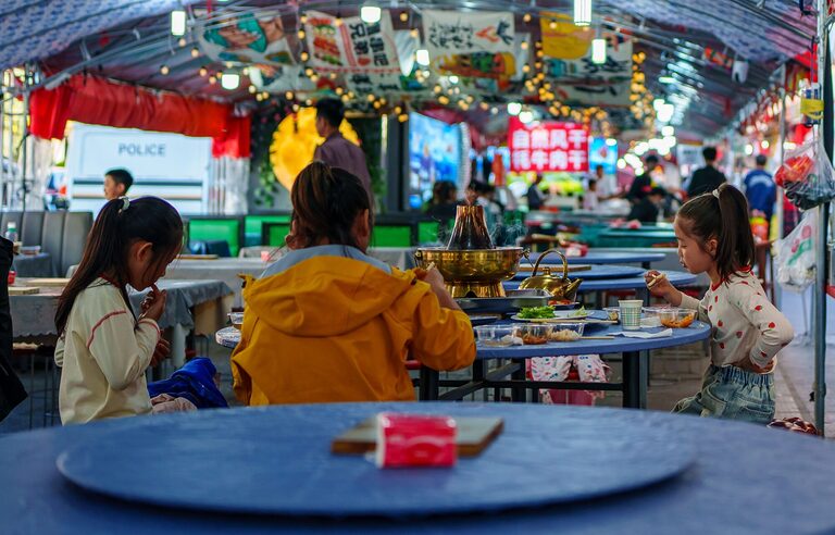 Children dining at a colourful street market in Qinghai, China, showcasing vibrant culture and traditional cuisine.