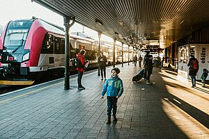 A young boy stands at a bustling urban railway station platform during daylight, capturing the essence of travel adventure.