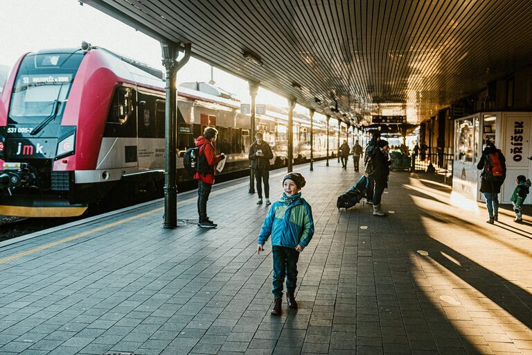 A young boy stands at a bustling urban railway station platform during daylight, capturing the essence of travel adventure.