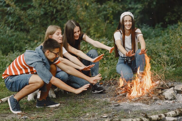 Group of teenagers enjoying a warm campfire during a camping trip in the outdoors.
