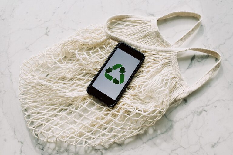 An eco-friendly message displayed on a smartphone resting on a reusable mesh bag, symbolising sustainability.