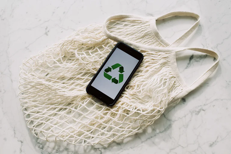 An eco-friendly message displayed on a smartphone resting on a reusable mesh bag, symbolising sustainability.