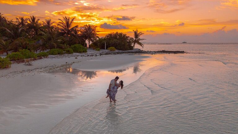 Couple romantic sunset walk on a budget-friendly beach honeymoon