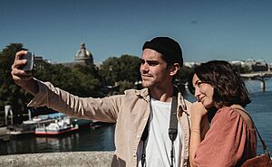 Couple enjoying a sunny day taking a selfie by the Seine River in Paris.