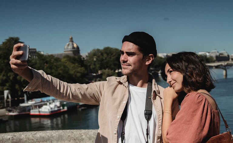 Couple enjoying a sunny day taking a selfie by the Seine River in Paris.